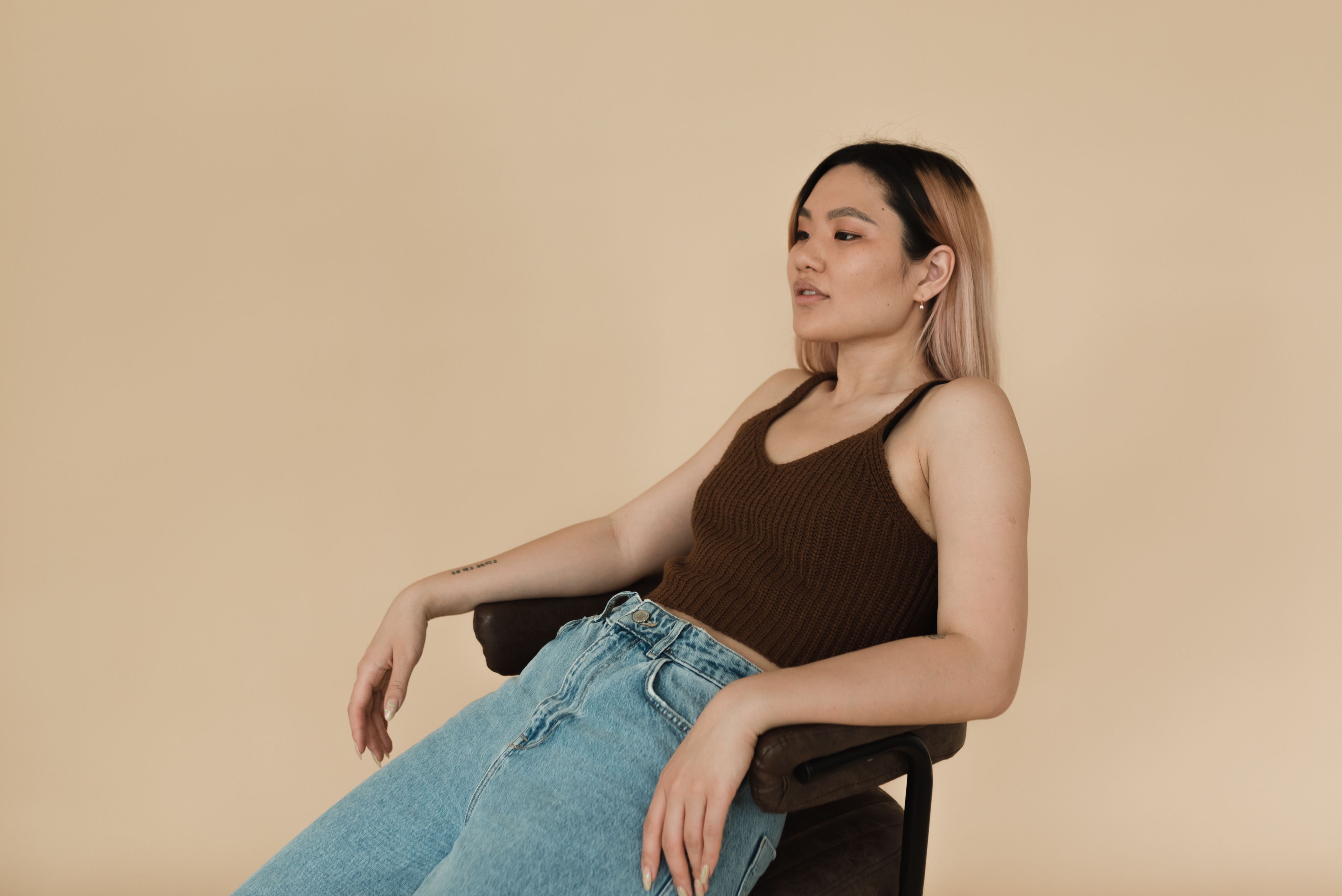 Elegant woman in casual attire sitting on a chair against a neutral background.