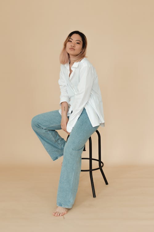 Woman in White Top and Denim Jeans Sitting on a Chair