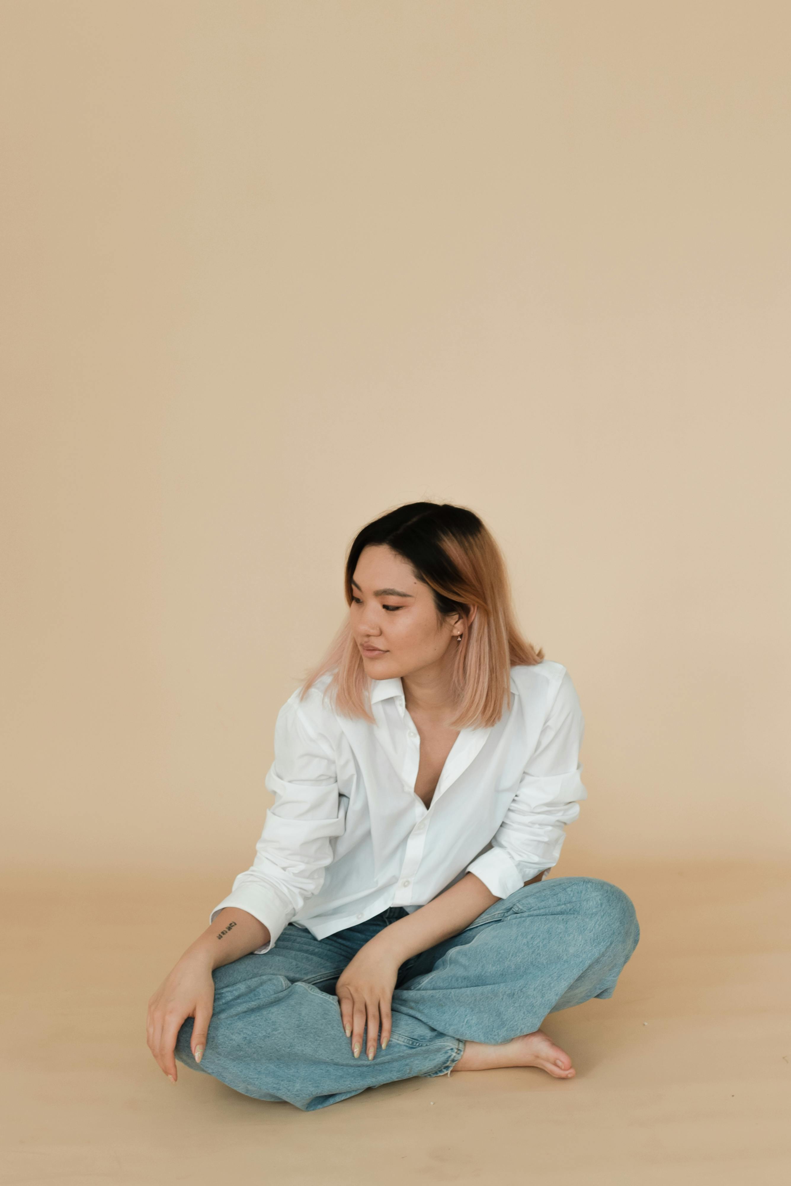 a woman in a dress shirt and denim jeans sitting on the floor