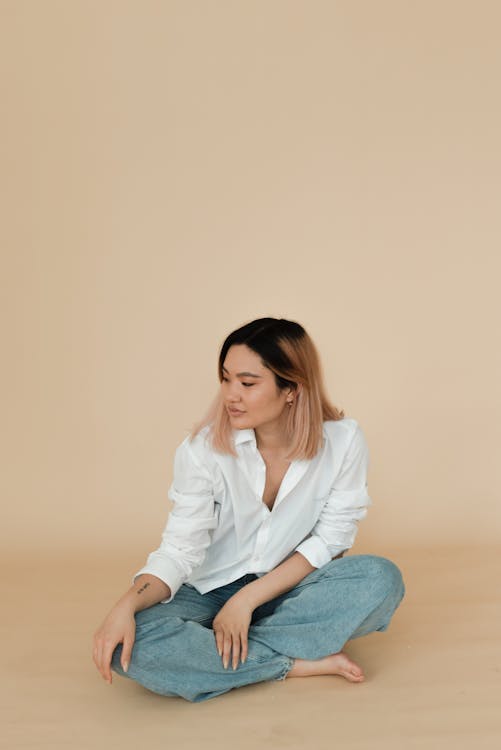 A Woman in a Dress Shirt and Denim Jeans Sitting on the Floor