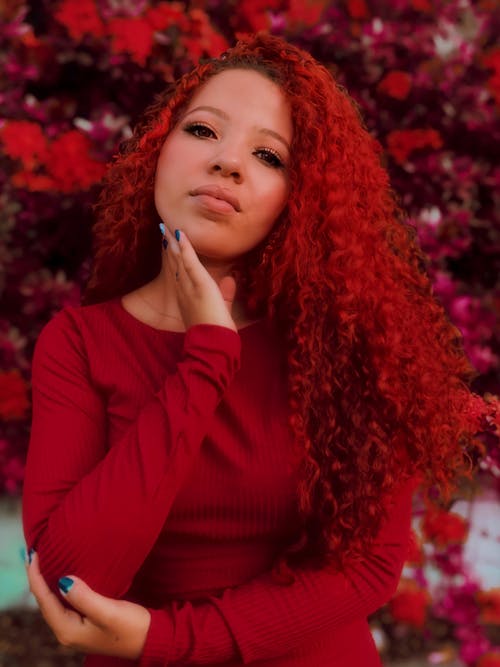 Black woman with red hair touching chin in garden