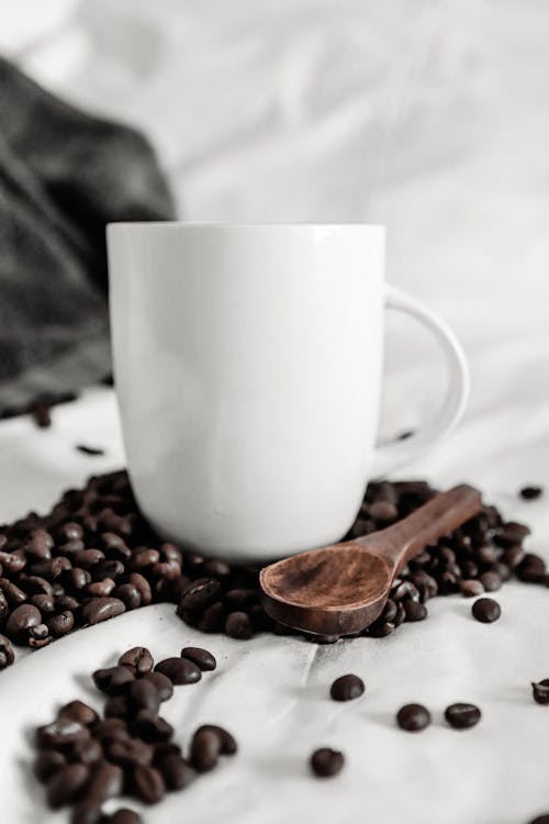 Coffee beans scattered on white cloth near cup