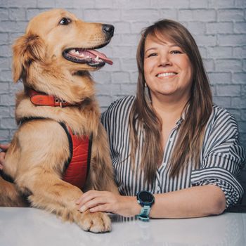 Smiling female in casual clothes with Golden Retriever dog with collar sitting at table in light room