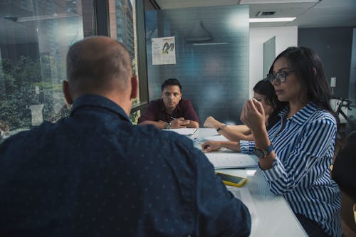 Group of young coworkers in casual clothes gathering around table with documents and discussing business project while working together in modern workspace