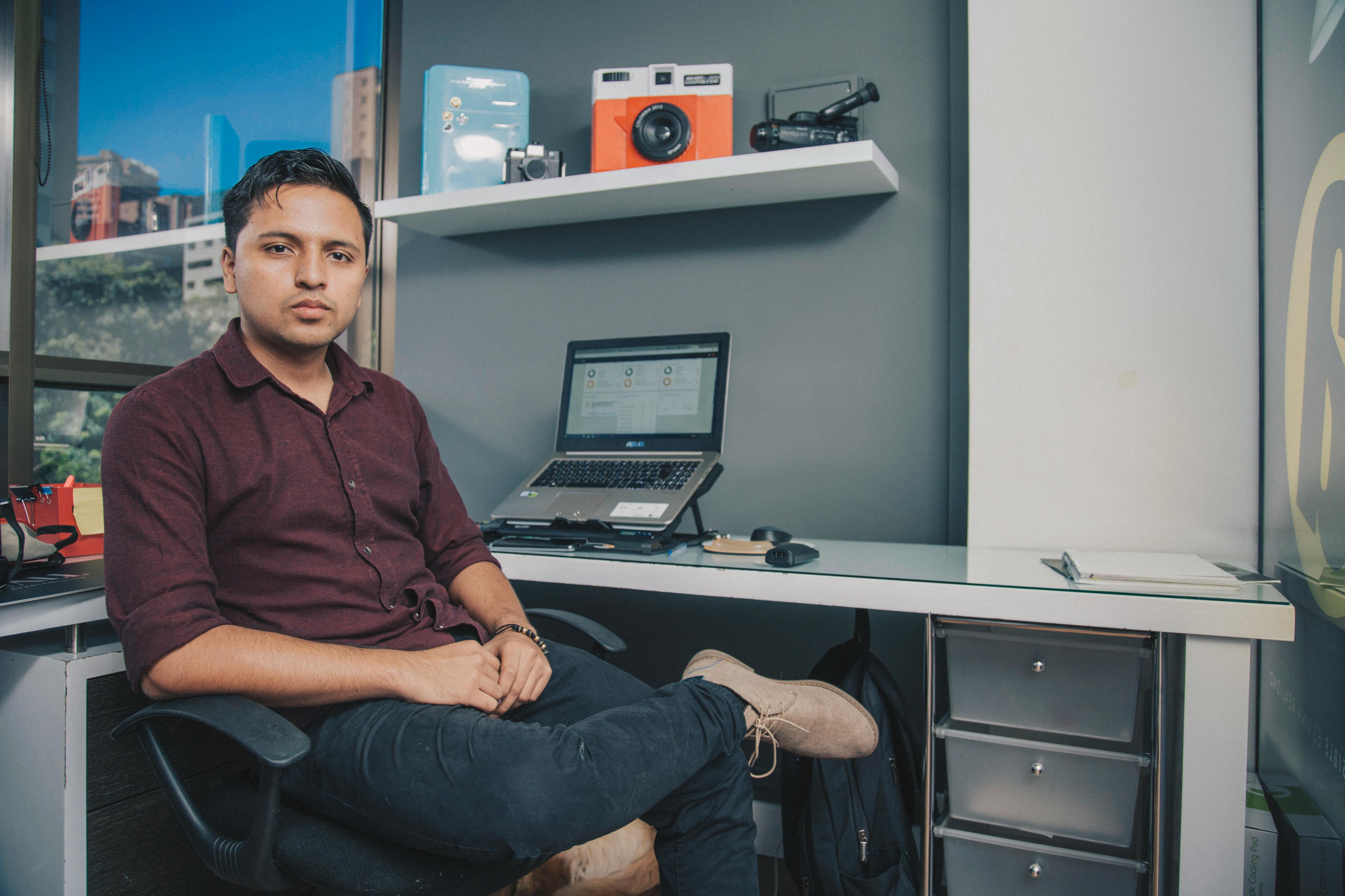Young entrepreneur sitting at office desk with laptop and gadgets, Antioquia, Colombia.