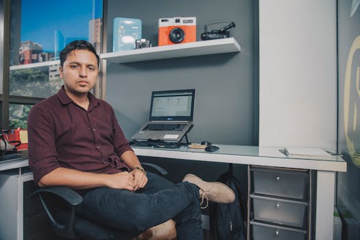 Young entrepreneur sitting at office desk with laptop and gadgets, Antioquia, Colombia.