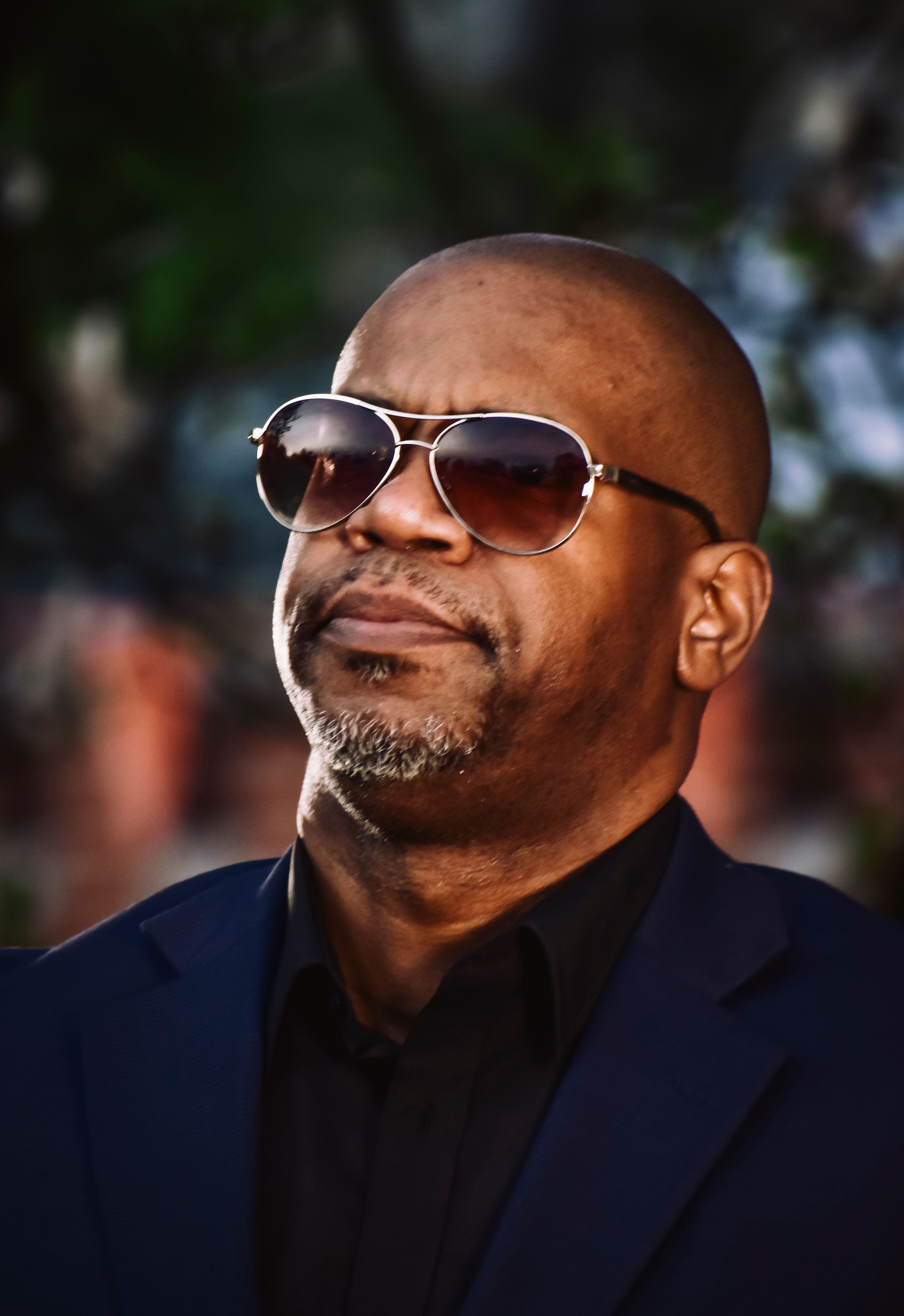 A confident bald man with sunglasses enjoying a bright day outdoors, exuding poise and style.
