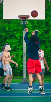 Men playing basketball outdoors with face shield during pandemic.