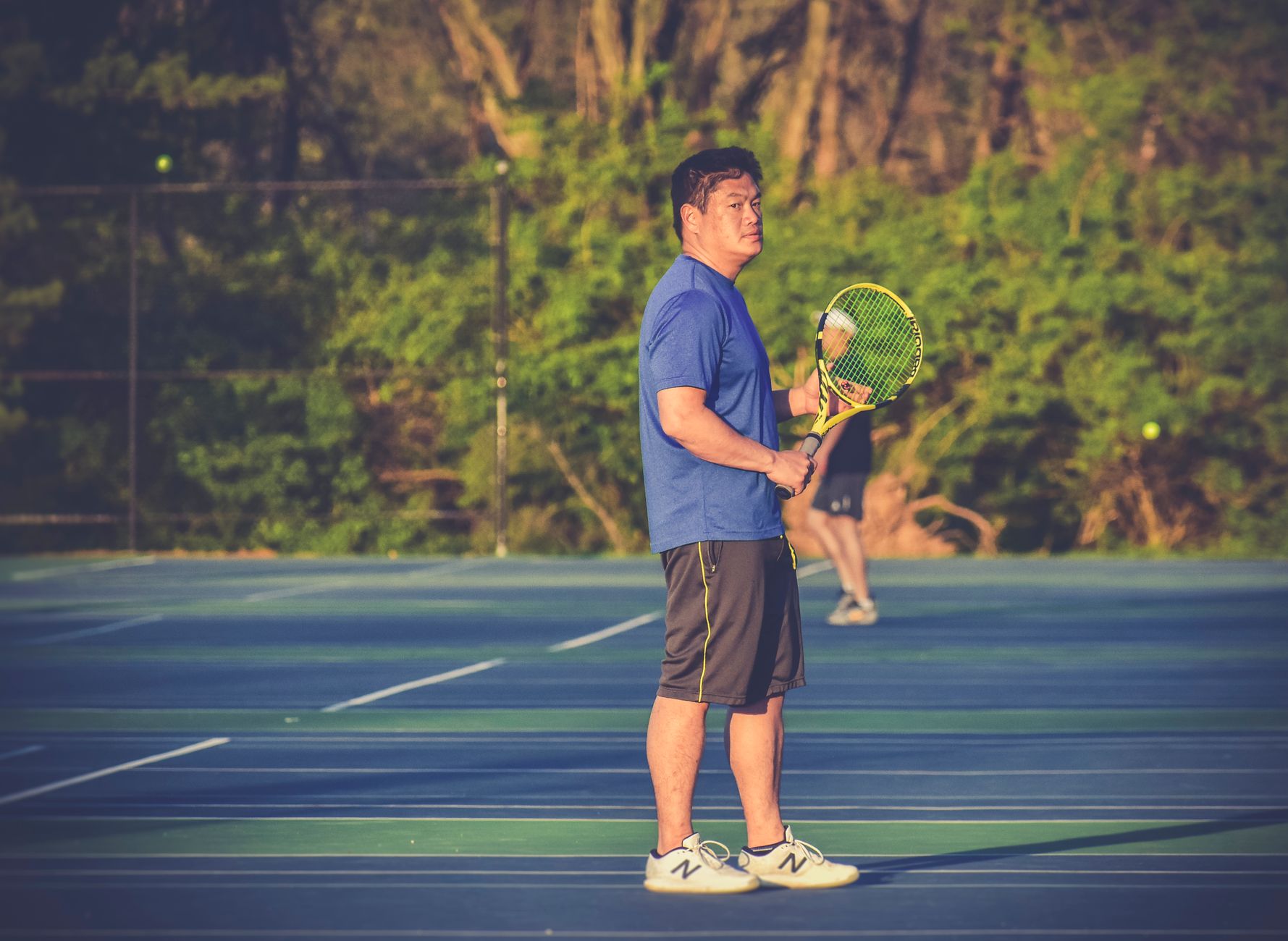 A man playing tennis on an outdoor court during the day, holding a racket.
