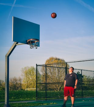 A young man enjoys playing basketball on an outdoor court under a clear sky.