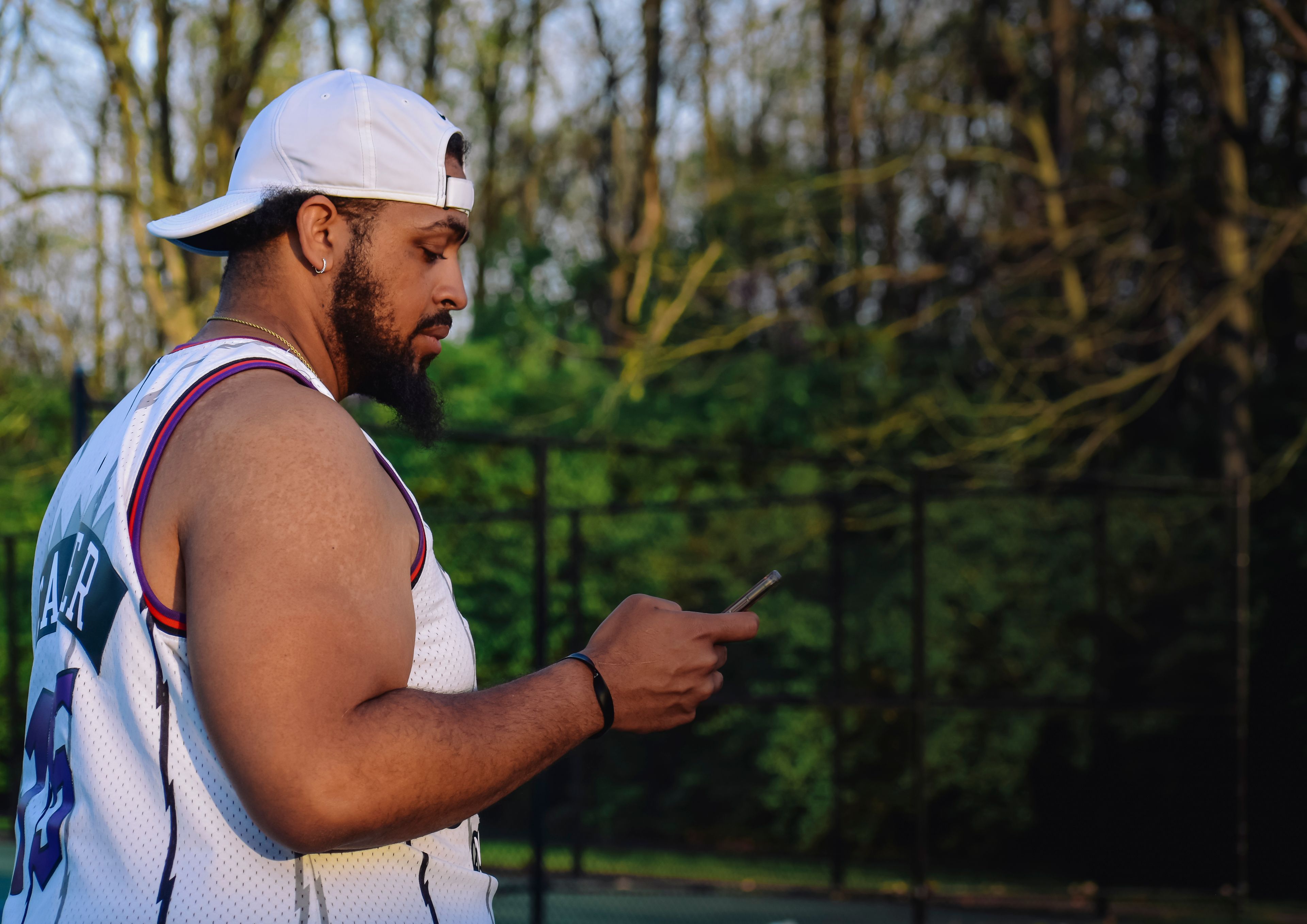 A man in sportswear checks his smartphone in a lush green park during daylight.