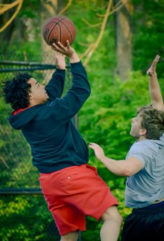Two young men playing an intense game of outdoor basketball during the day.