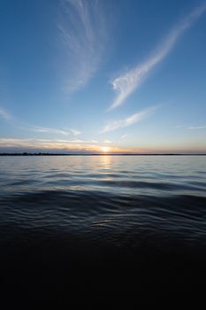 Peaceful sunset over a calm ocean with rippling water and wispy clouds.