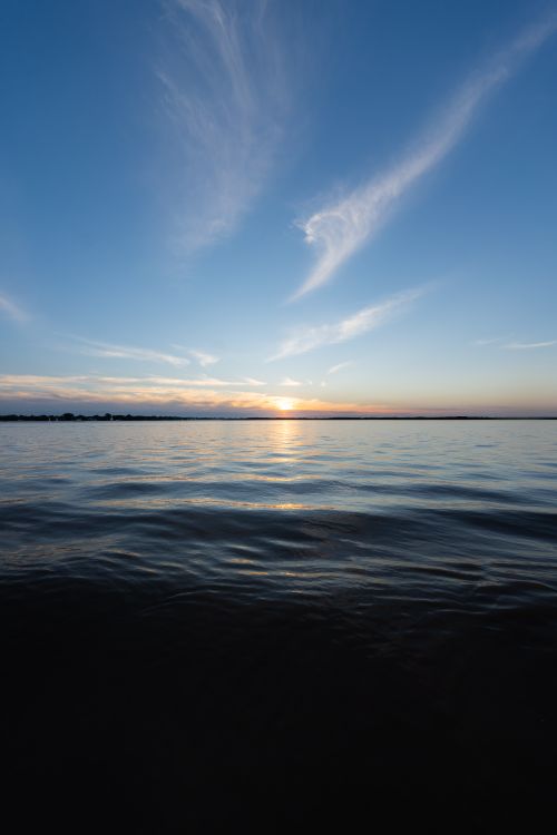 A sunset over the water with clouds in the sky · Free Stock Photo