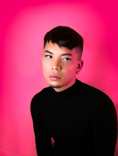 Thoughtful young man with makeup looking away in pink studio