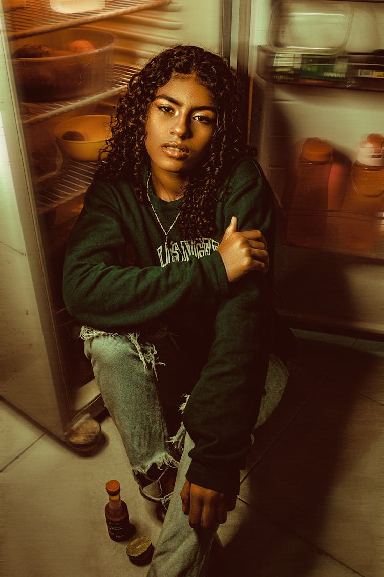 A Young Woman Sitting By An Open Fridge