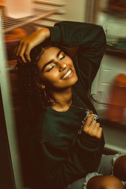 A joyful adult woman leans against an open refrigerator, eyes closed and smiling warmly.