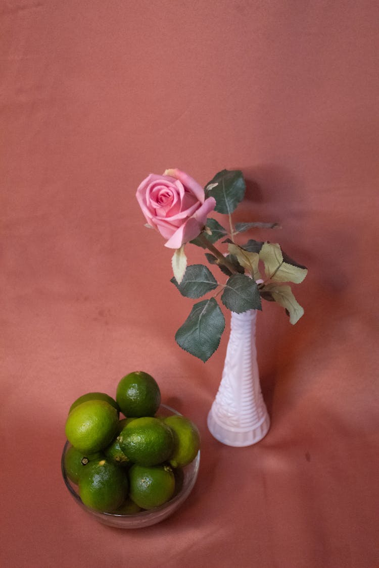 Pink Rose On Ceramic Vase Beside A Bowl Of Fresh Limes