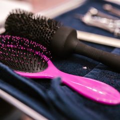 Hot-pink oval detangling brush with a black bristle pad lying beside a black round brush on a navy towel