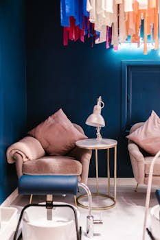 Modern salon waiting area featuring stylish armchairs and a decorative side table with a lamp.