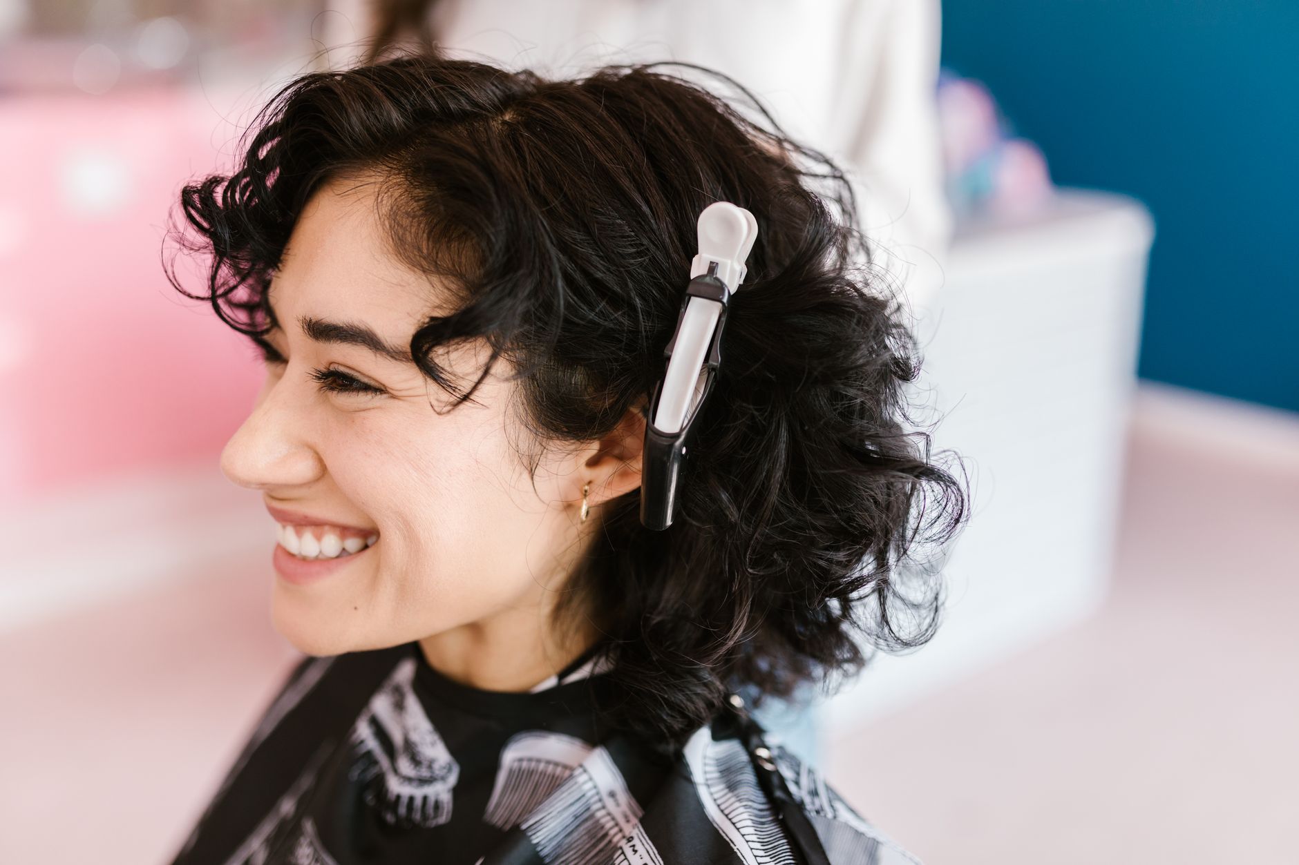 Side profile of a woman with curly hair smiling in a hair salon with a hair clip.