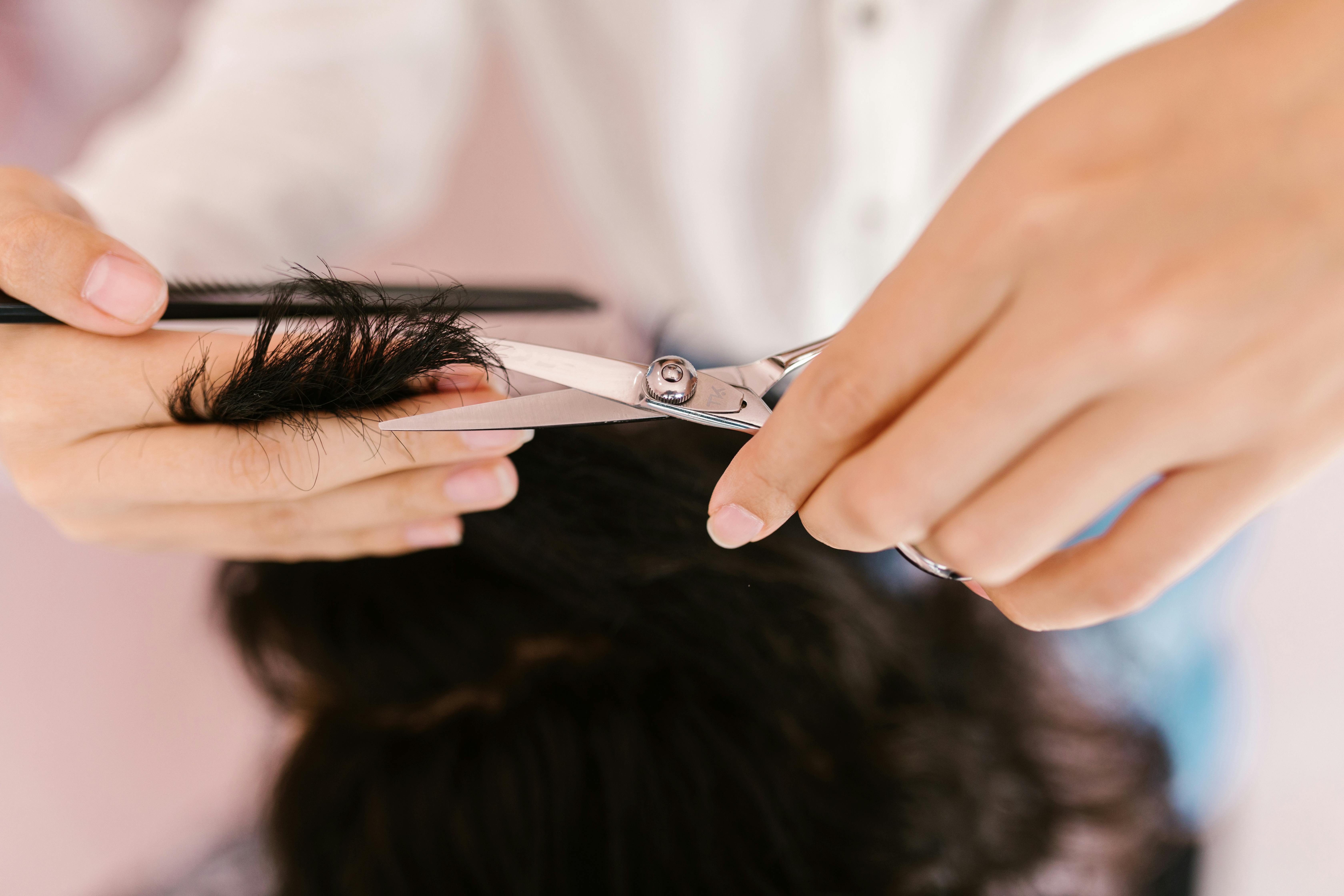 person holding silver scissors cutting hair