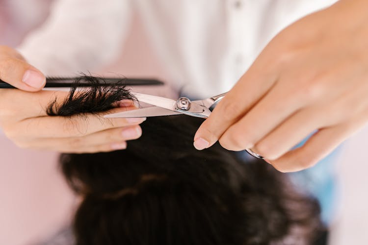 Person Cutting Hair Using A Silver Scissors