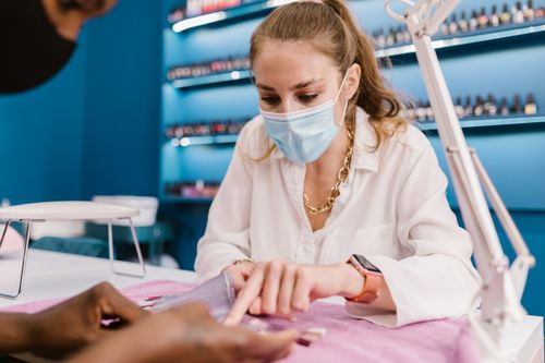 Free A young woman wearing a mask provides a manicure service in a modern salon setting. Stock Photo