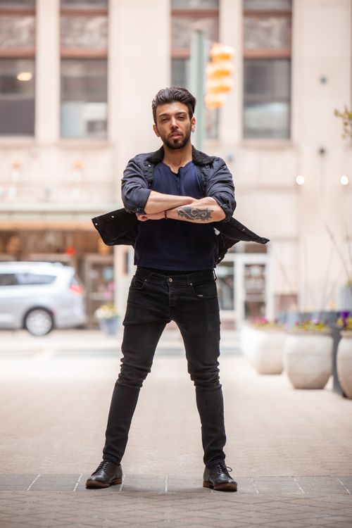 Free Confident man with tattooed arm stands on urban street with arms crossed. Casual fashion and modern city backdrop. Stock Photo