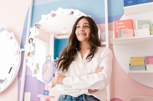Free Confident woman in a chic hair salon with colorful decor, arms crossed and smiling. Stock Photo