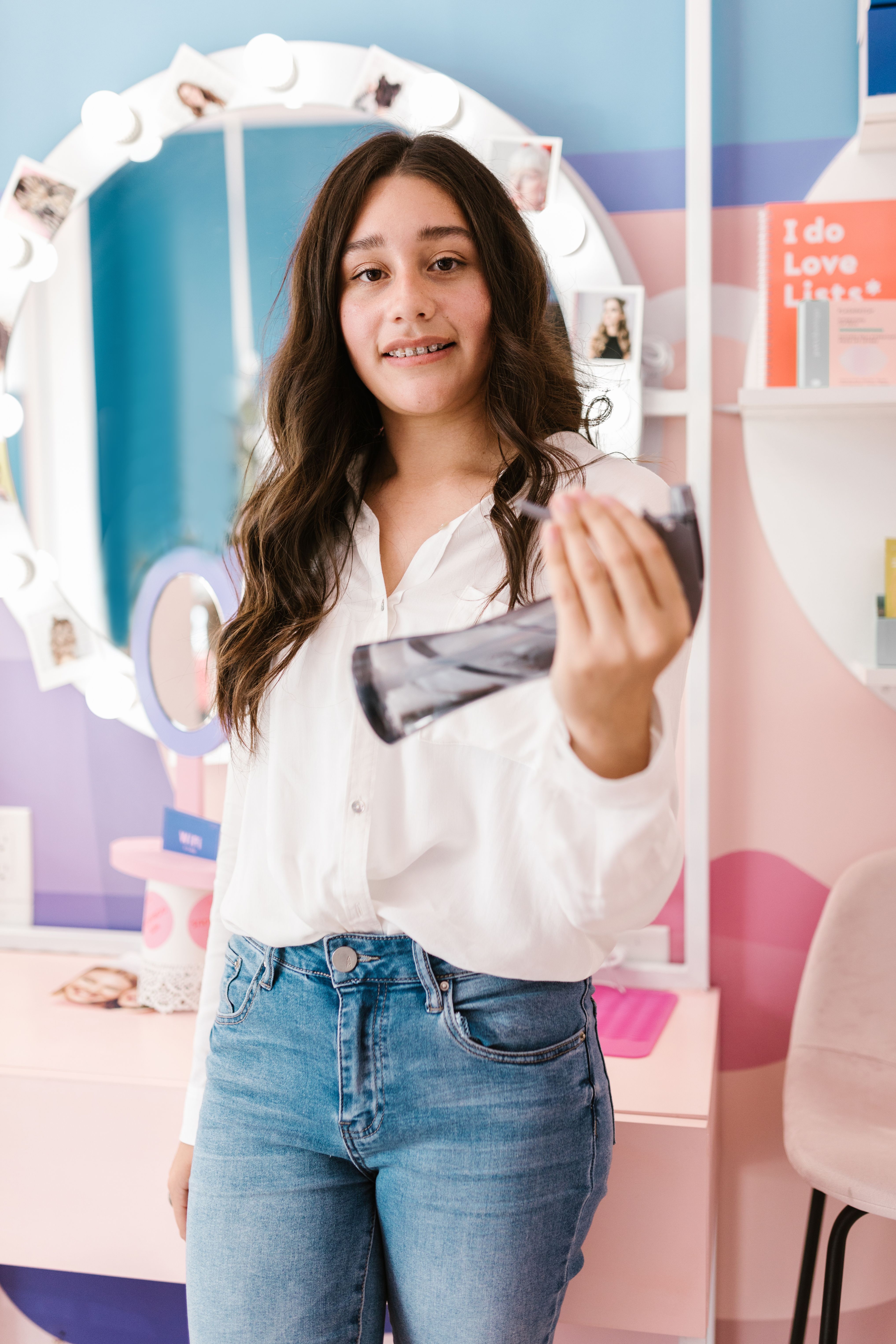 Smiling young woman holding a hair spray bottle in a colorful salon.