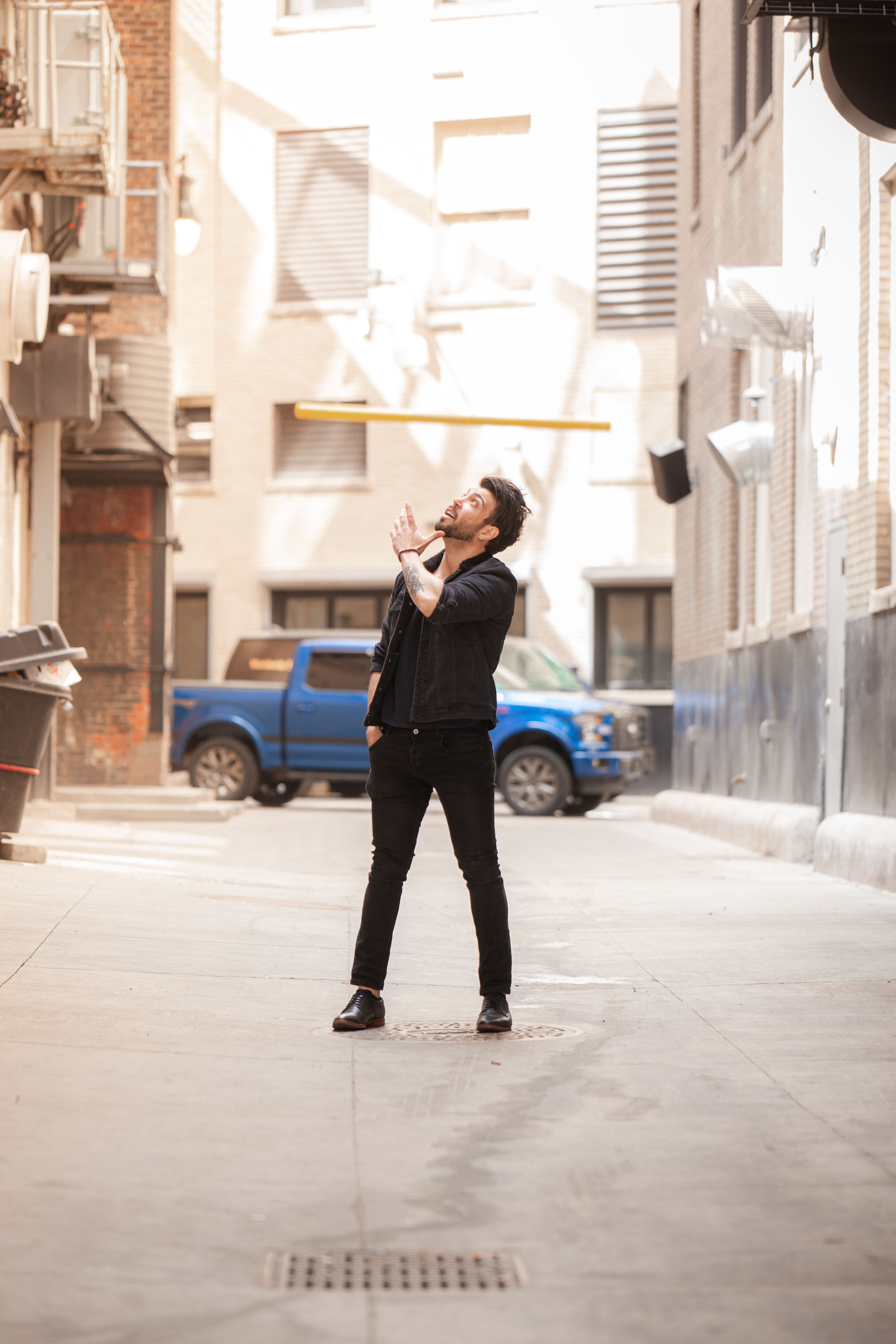 Man in black jacket standing in a city alley looking up. Urban lifestyle captured in daylight.