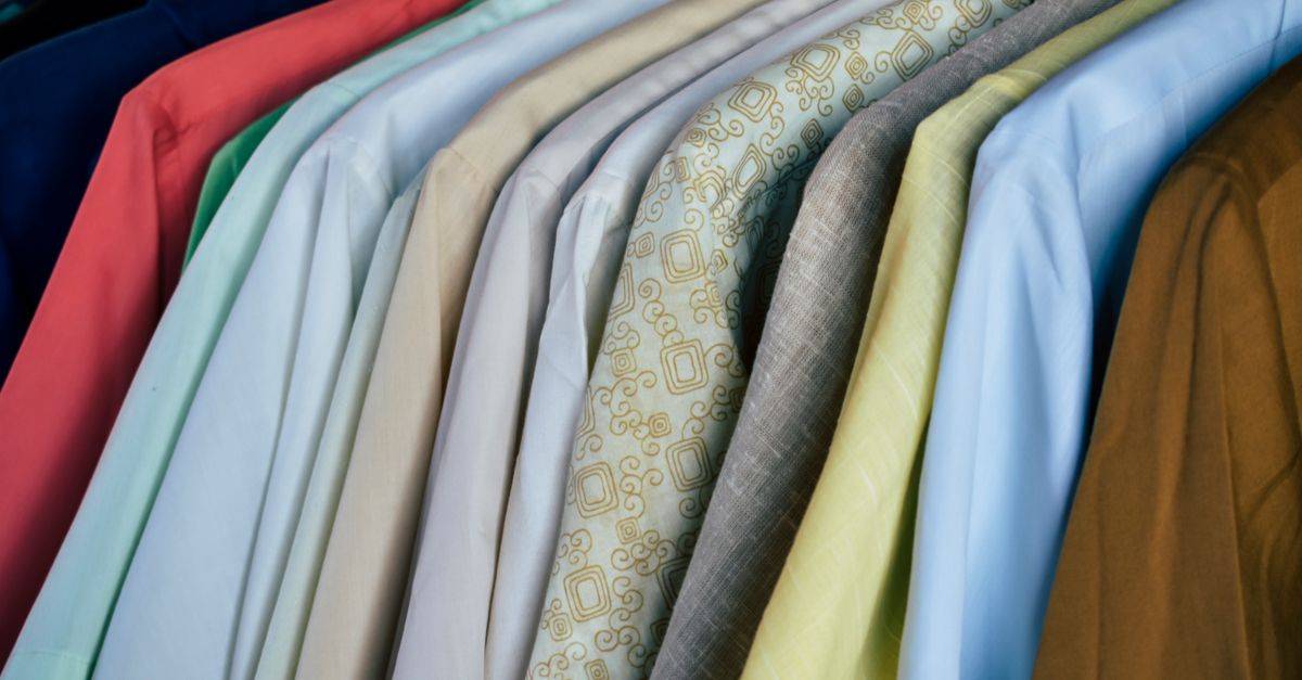 Uma variedade de camisas coloridas penduradas ordenadamente em cabides de madeira, exibindo diferentes tecidos.