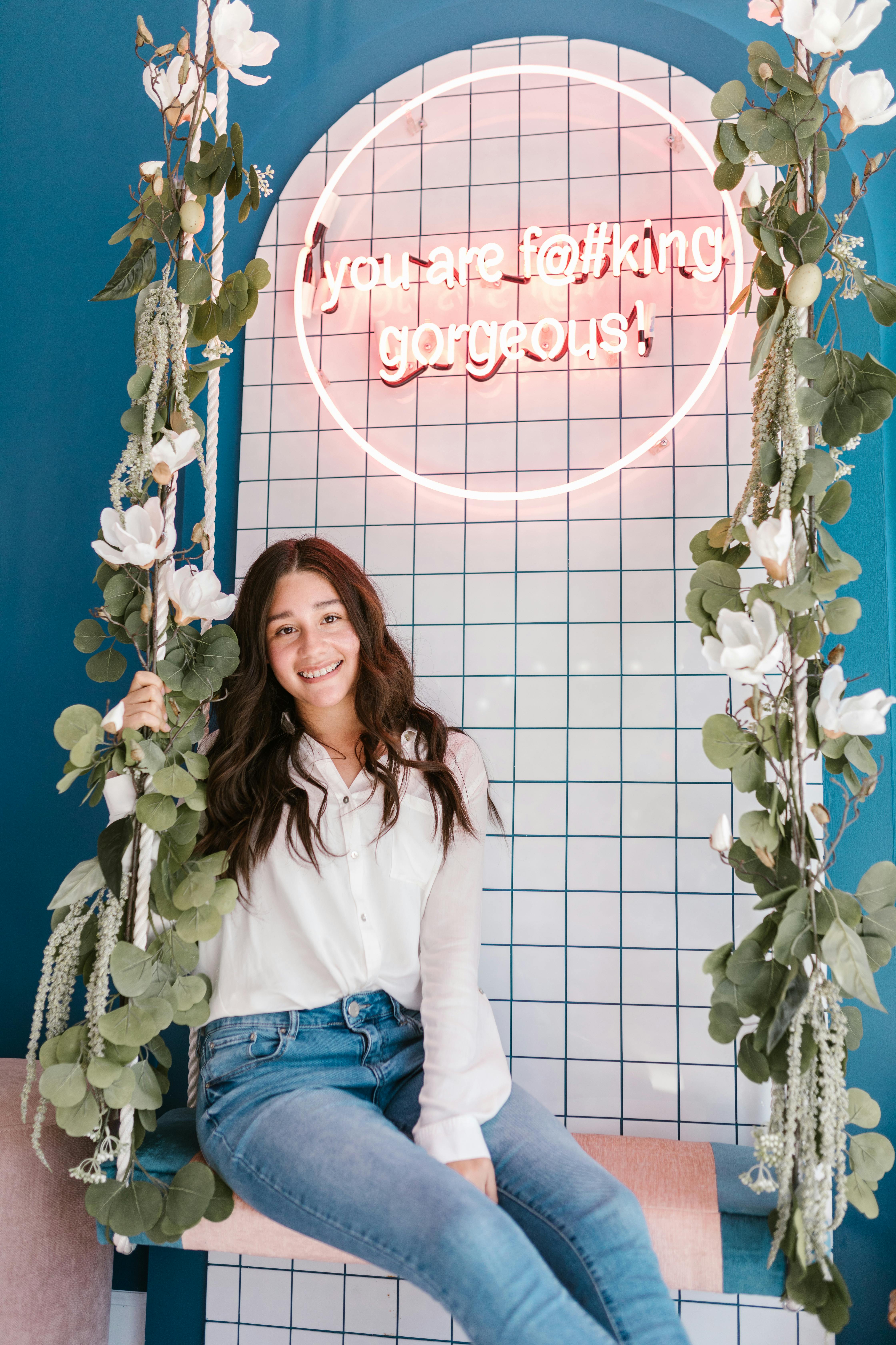 woman in white dress shirt and blue denim jeans standing beside green and white floral curtain