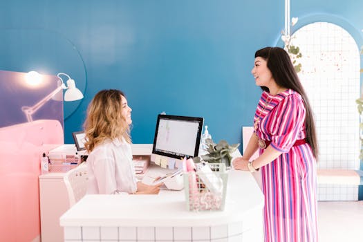 Two women engaging in a lively conversation at a stylish salon reception area.