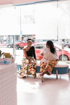 Two women in colorful outfits enjoying conversation in a stylish salon.