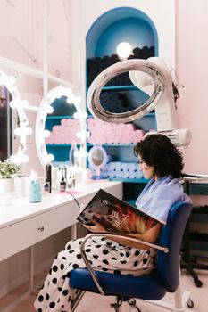 Woman enjoys reading in a stylish hair salon surrounded by beauty products.