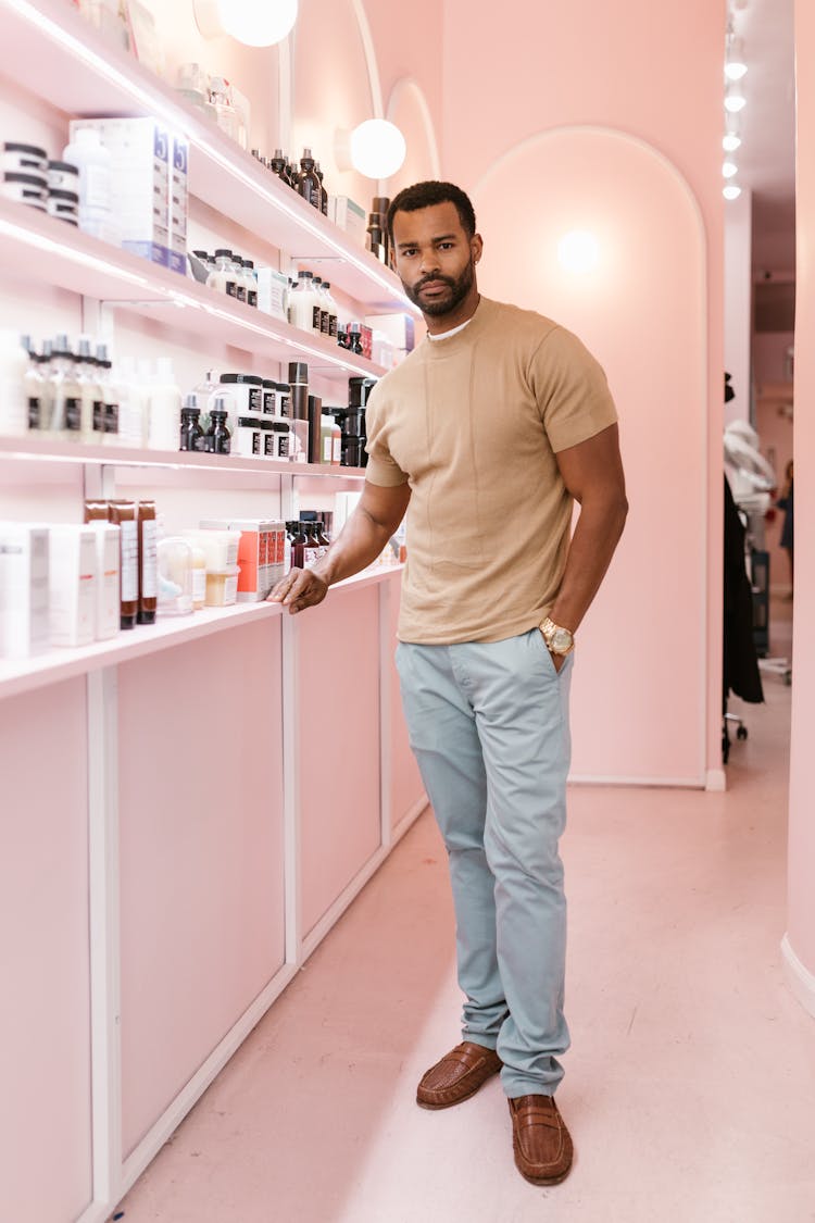 A Man Posing Beside A Shelf With Assorted Beauty Products