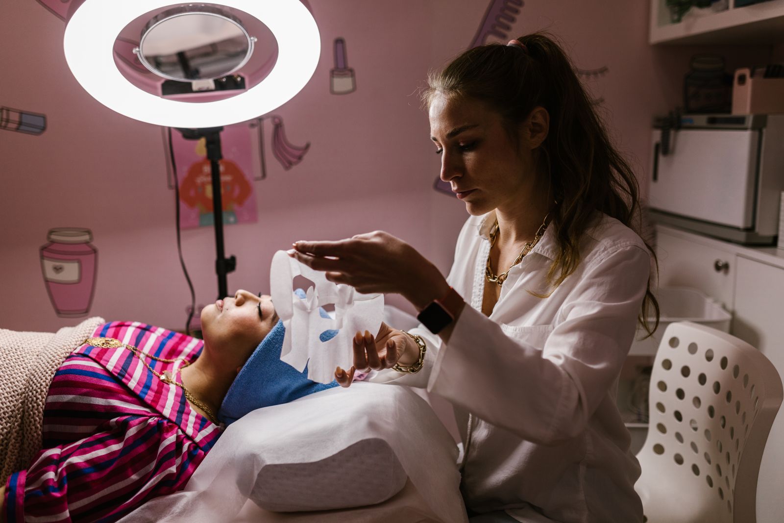 Esthéticienne appliquant un masque sur le visage d'une cliente allongée en cabine d'institut, lumière tamisée