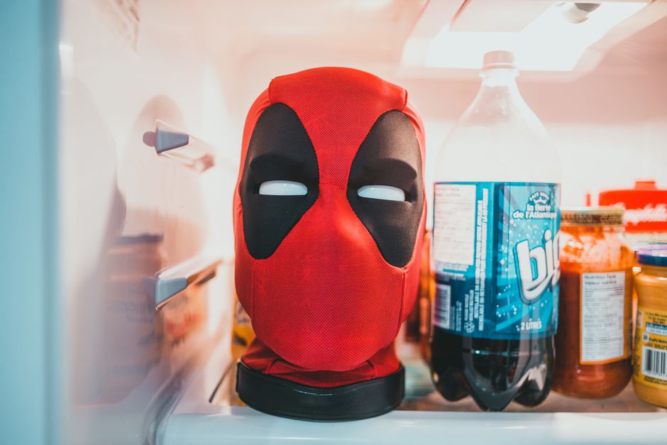 A humorous view of a red mask inside a refrigerator among bottles and jars.