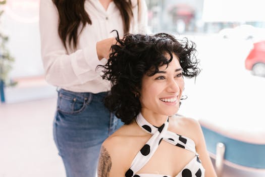 Joyful woman with curly hair being styled in a modern salon setting.