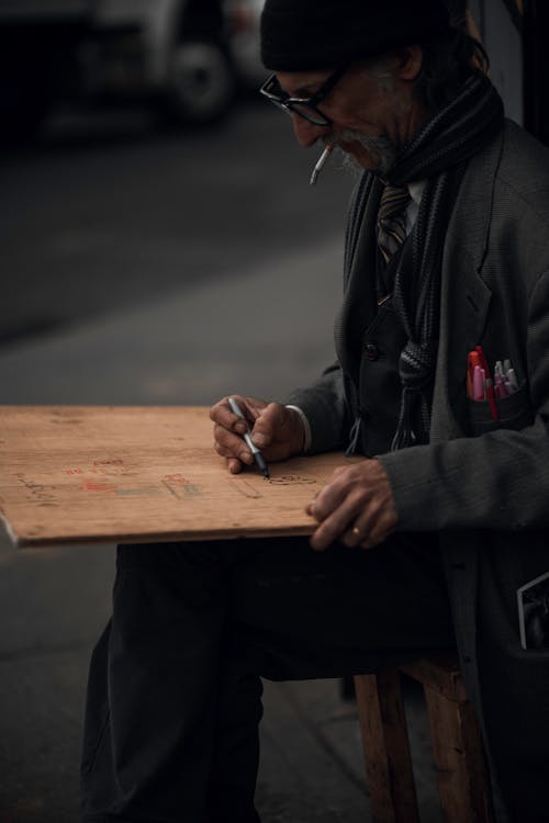 An Elderly Man Smoking a Cigarette Drawing on a Wood Board 