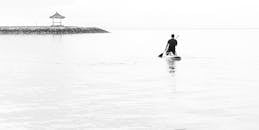 Man in Black Wet Suit Riding on White Surfboard on Sea