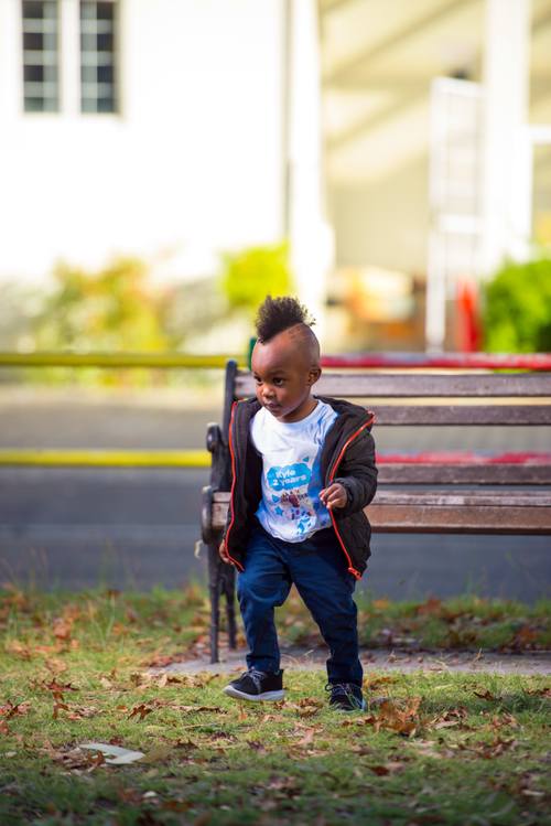 Free Stylish child with mohawk exploring near a park bench on a sunny day, showcasing vibrant style and energy. Stock Photo