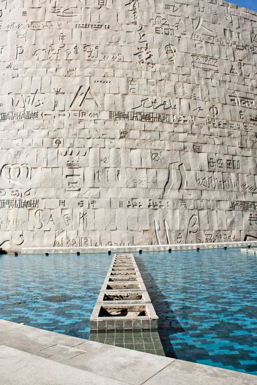 Free Stone wall with ancient script carvings and water feature in daylight ambiance. Stock Photo