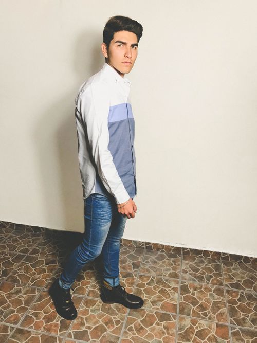 Free Young man posing indoors in a stylish casual outfit featuring denim jeans and a trendy shirt. Stock Photo