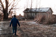 一个身穿蓝色夹克的小男孩走向冬季乡村里的一座废弃谷仓