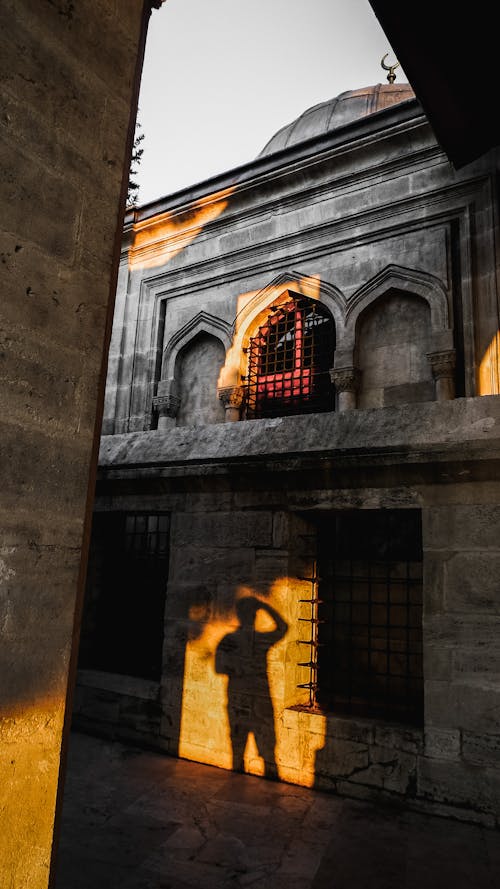 Shadow of unrecognizable male traveler on aged historic stone mosque with dome located on street of old town in sunny weather