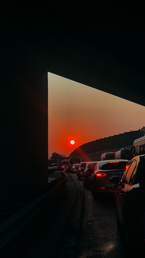 Through from tunnel of many modern automobiles driving in traffic jam at sundown time against bright sun shining on sky