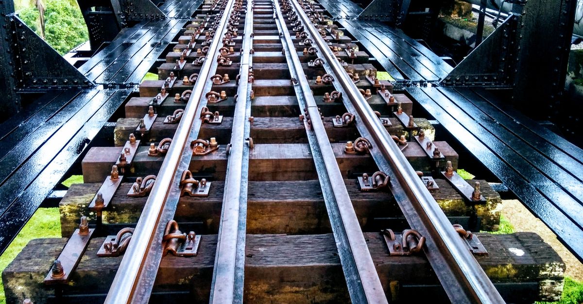 Photo by H H A striking perspective of metal railway tracks through an iron bridge in daylight.